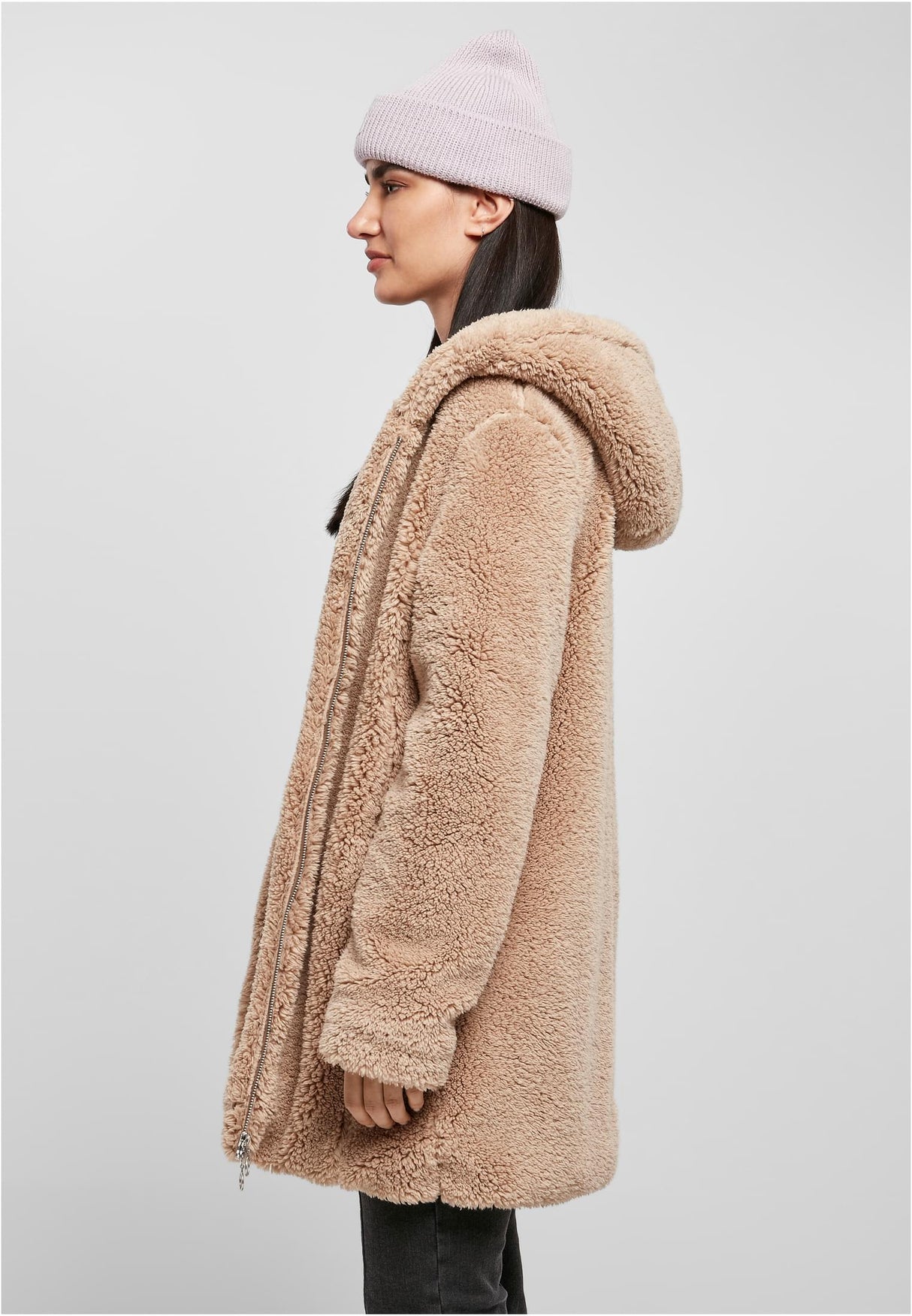 Sidoprofil av en kvinna som bär en beige UC Sherpa Jacket med huva och en ljuslila mössa.
