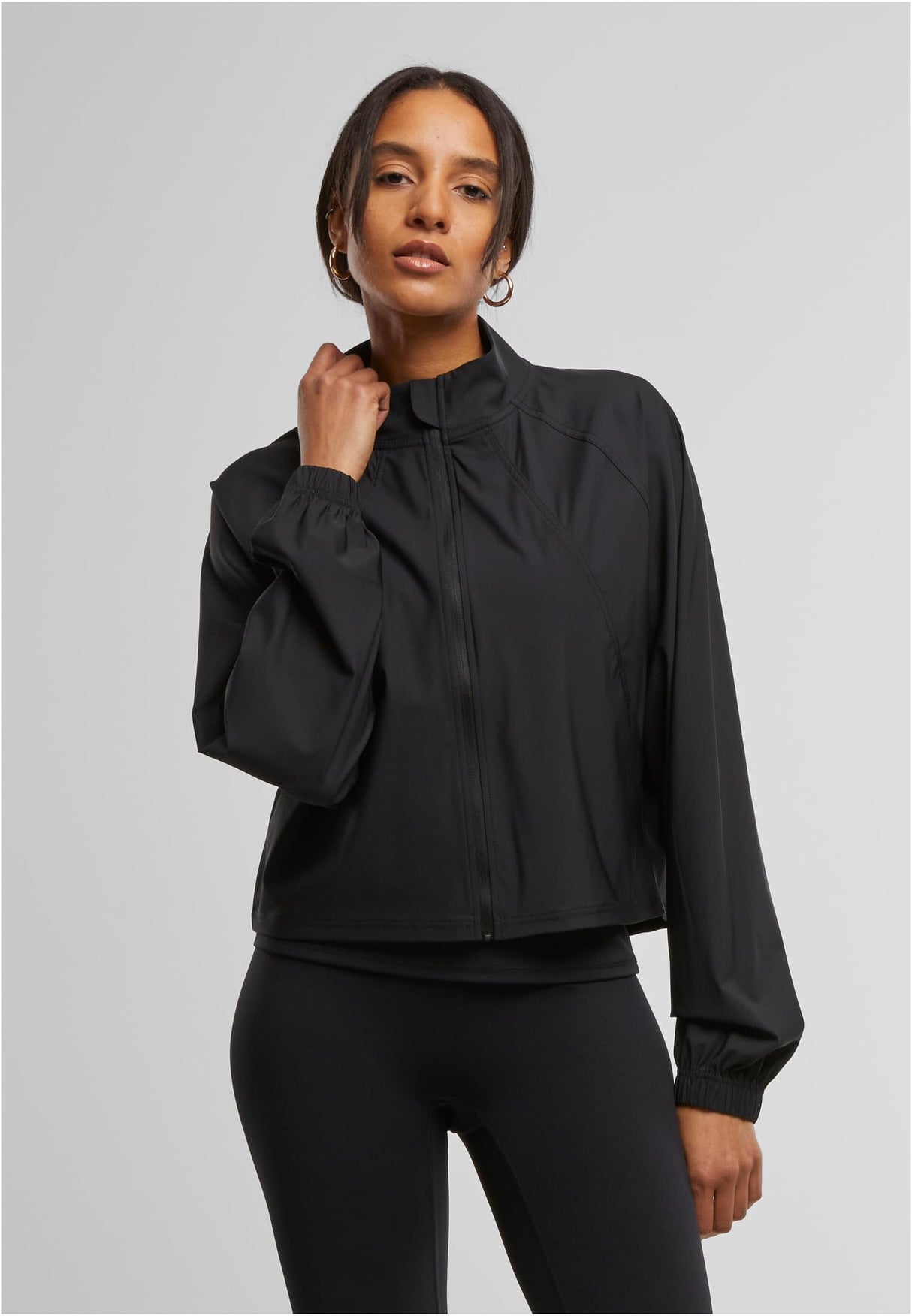 En kvinna visar framsidan av den svarta sportjackan UC Sports Jacket.