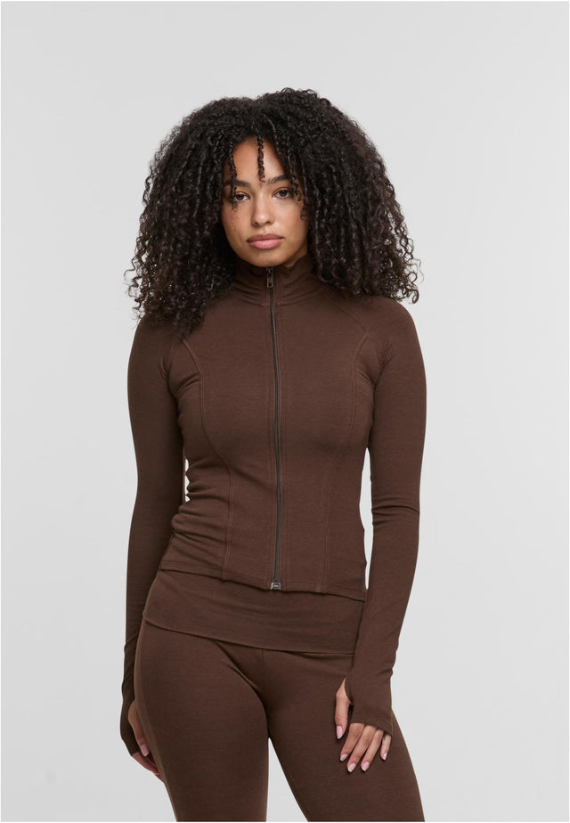 En kvinna visar framsidan av en brun, åtsittande träningsjacka med dragkedja.