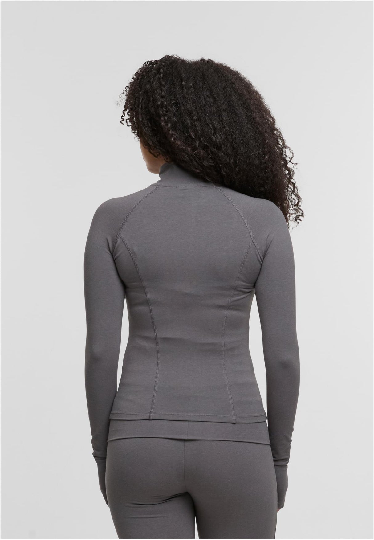 En kvinna visar baksidan av en grå, långärmad och figurnära träningsjacka.