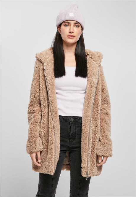 En kvinna bär en beige UC Sherpa Jacket öppen, med ett vitt linne, svarta jeans och en ljuslila mössa.