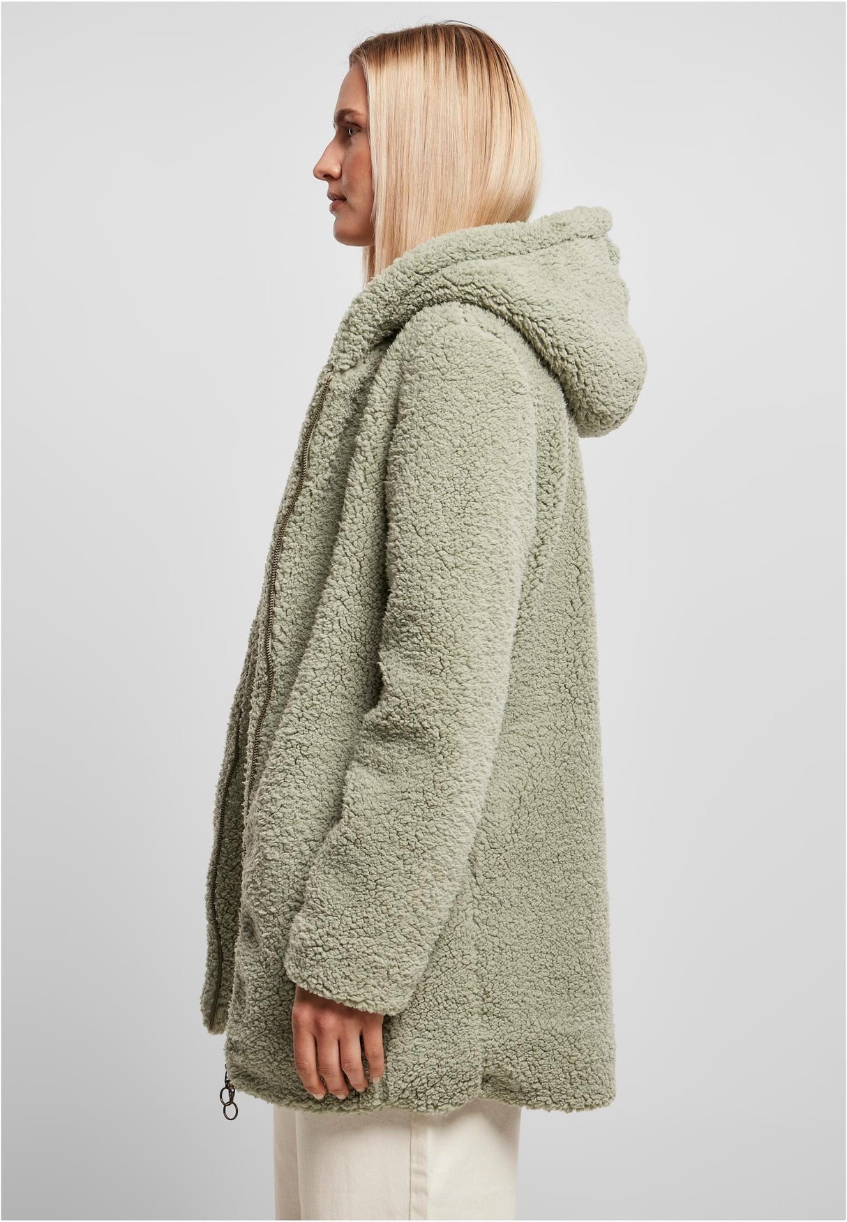 En kvinna i profil som bär en grön, luddig sherpajacka med huva.